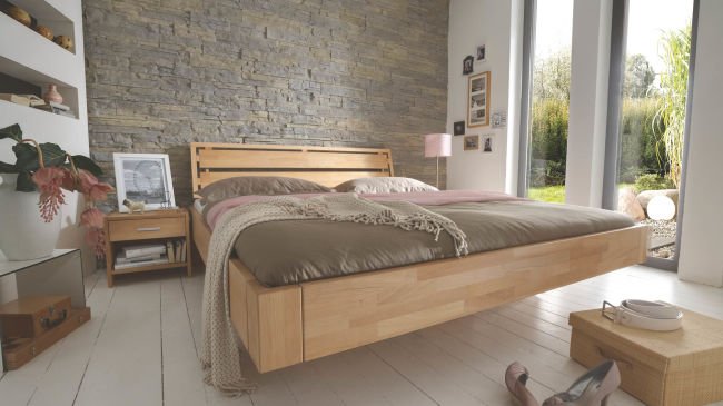 schwebendes Bett in brauntönen vor Steinwand